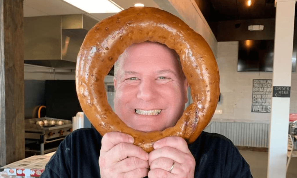 Chef Adam proudly presenting his signature bagel at Meshugana Deli, Sarasota, a testament to culinary passion and tradition.